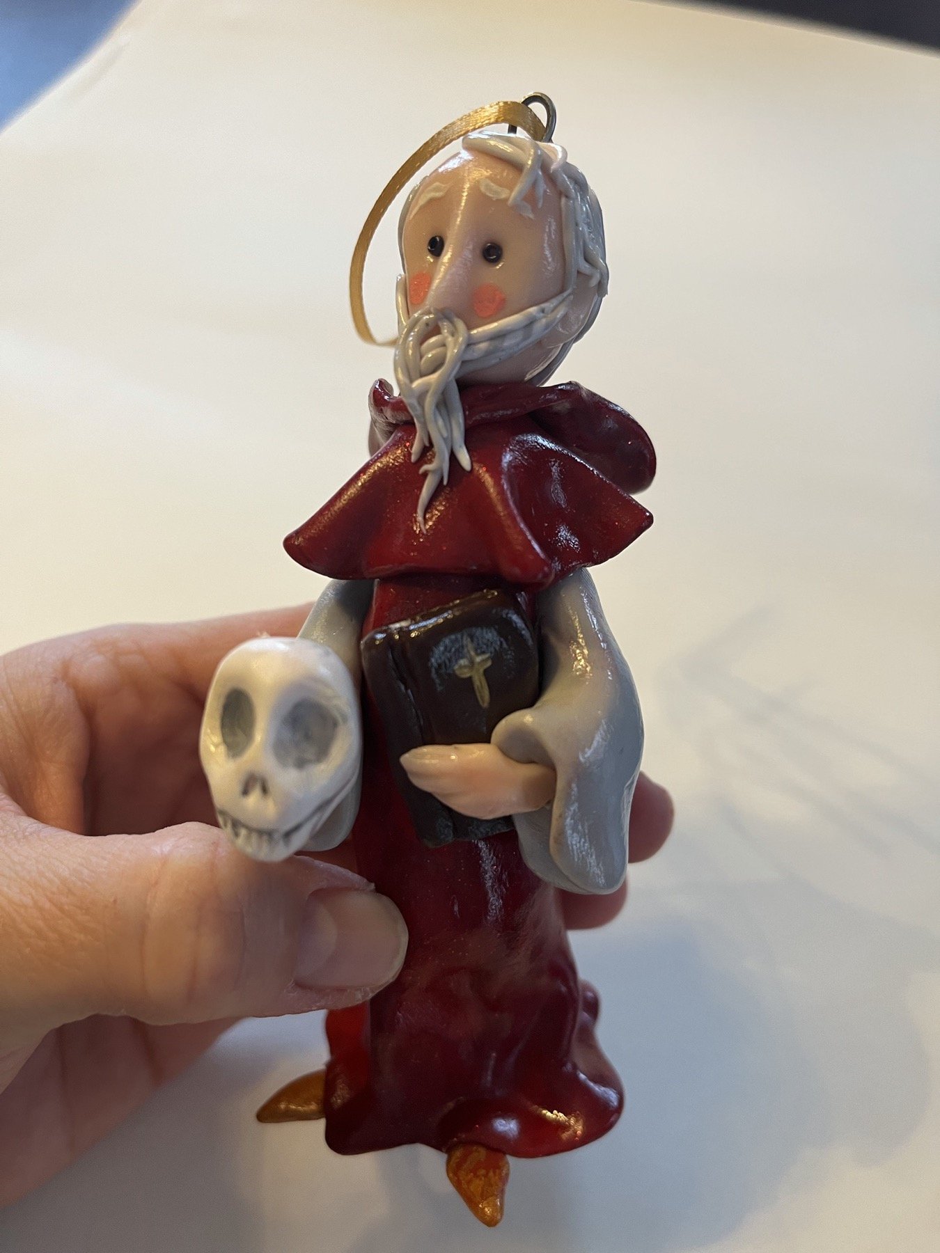 Front view of a hand-sculpted saint figure holding symbolic objects